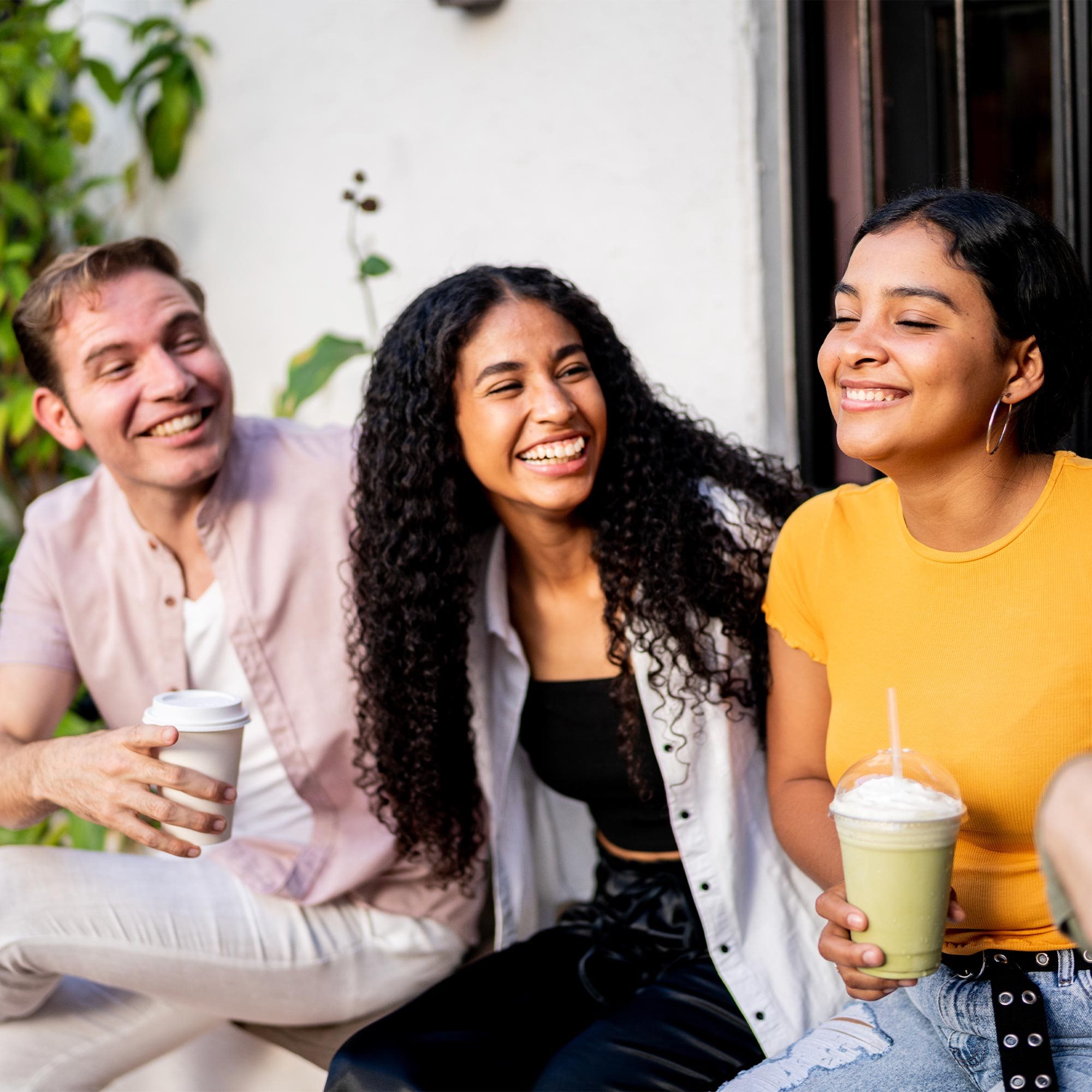 Three friends sitting together while drinking coffee and smiling.