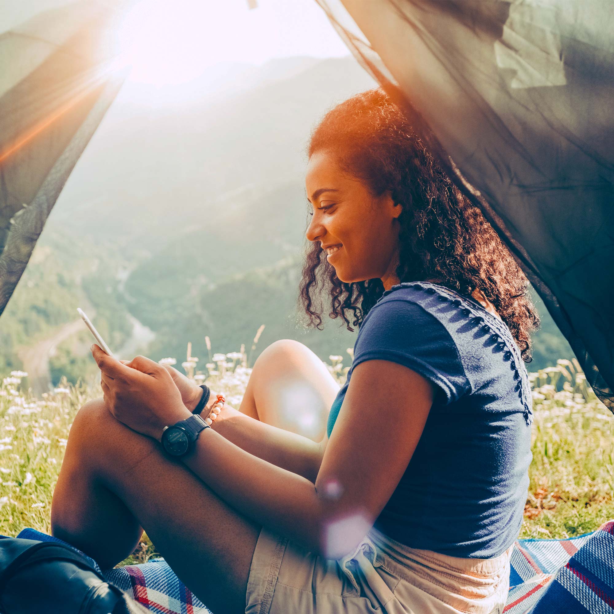 A woman sits in her tent overlooking the valley as she smiles at her cell phone.