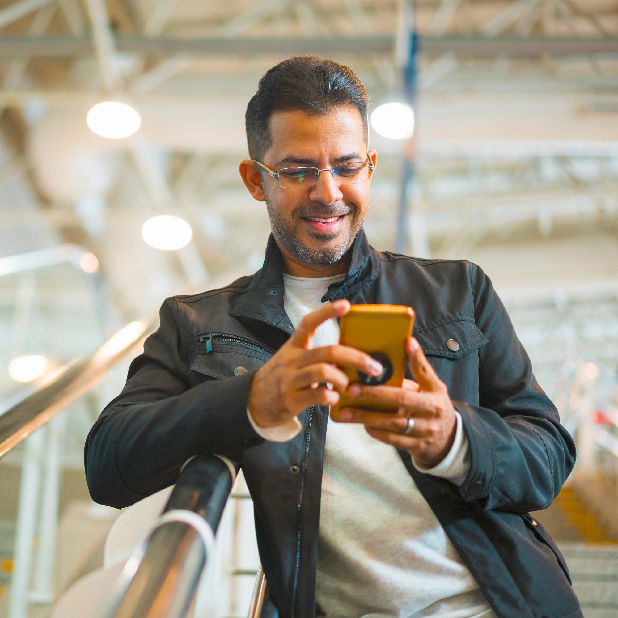 A man standing on the stairs smiles and looks at his cell phone.