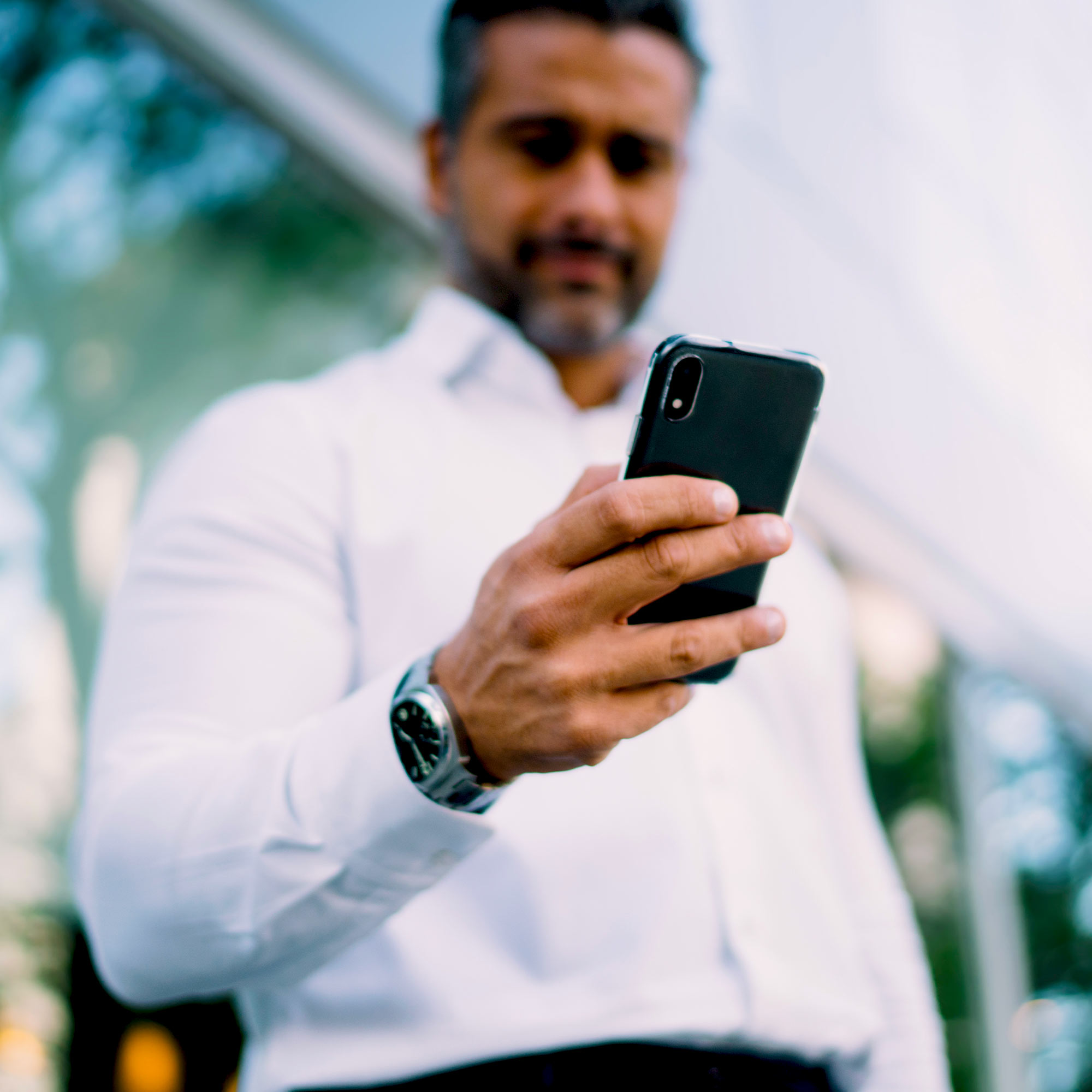 A man wearing a watch and white button up shirt is looking down at his phone.