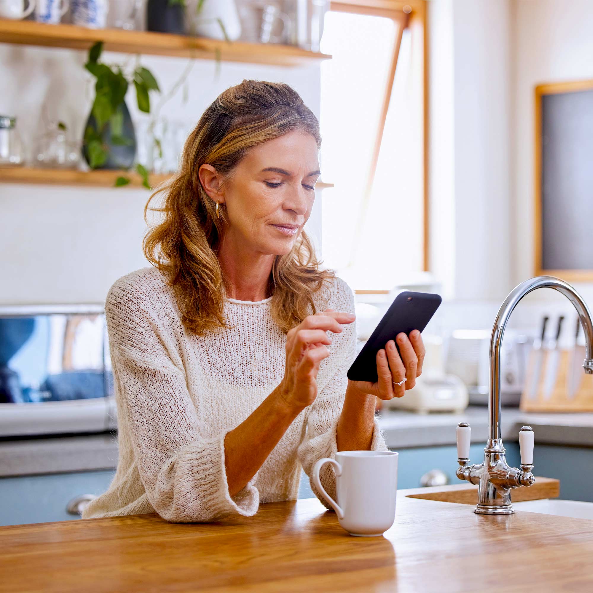 A woman sitting at the kitchen island and using her cell phone.