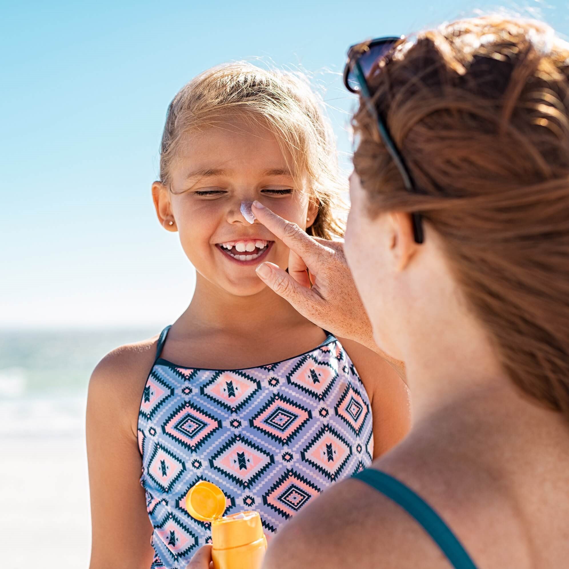 Woman putting sunscreen on her child's nose as she giggles.