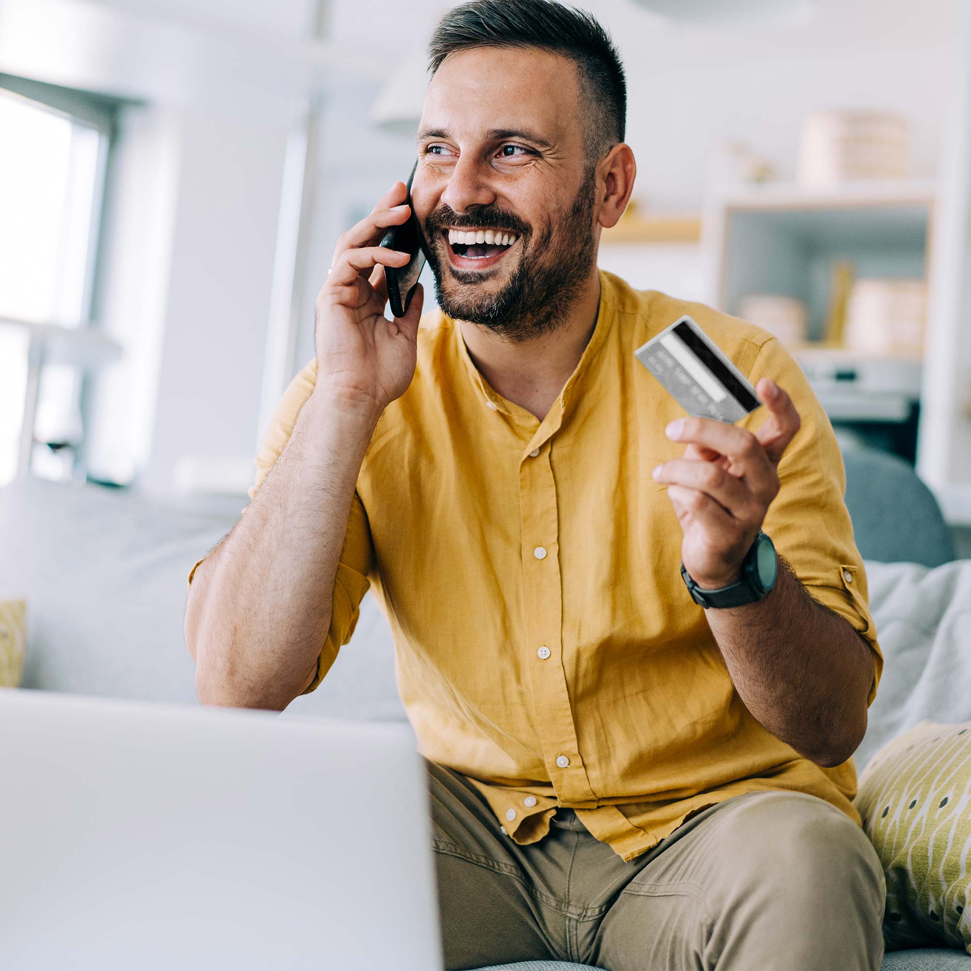 Woman looking and smiling at her debit card and ipad as she reclines on the sofa.