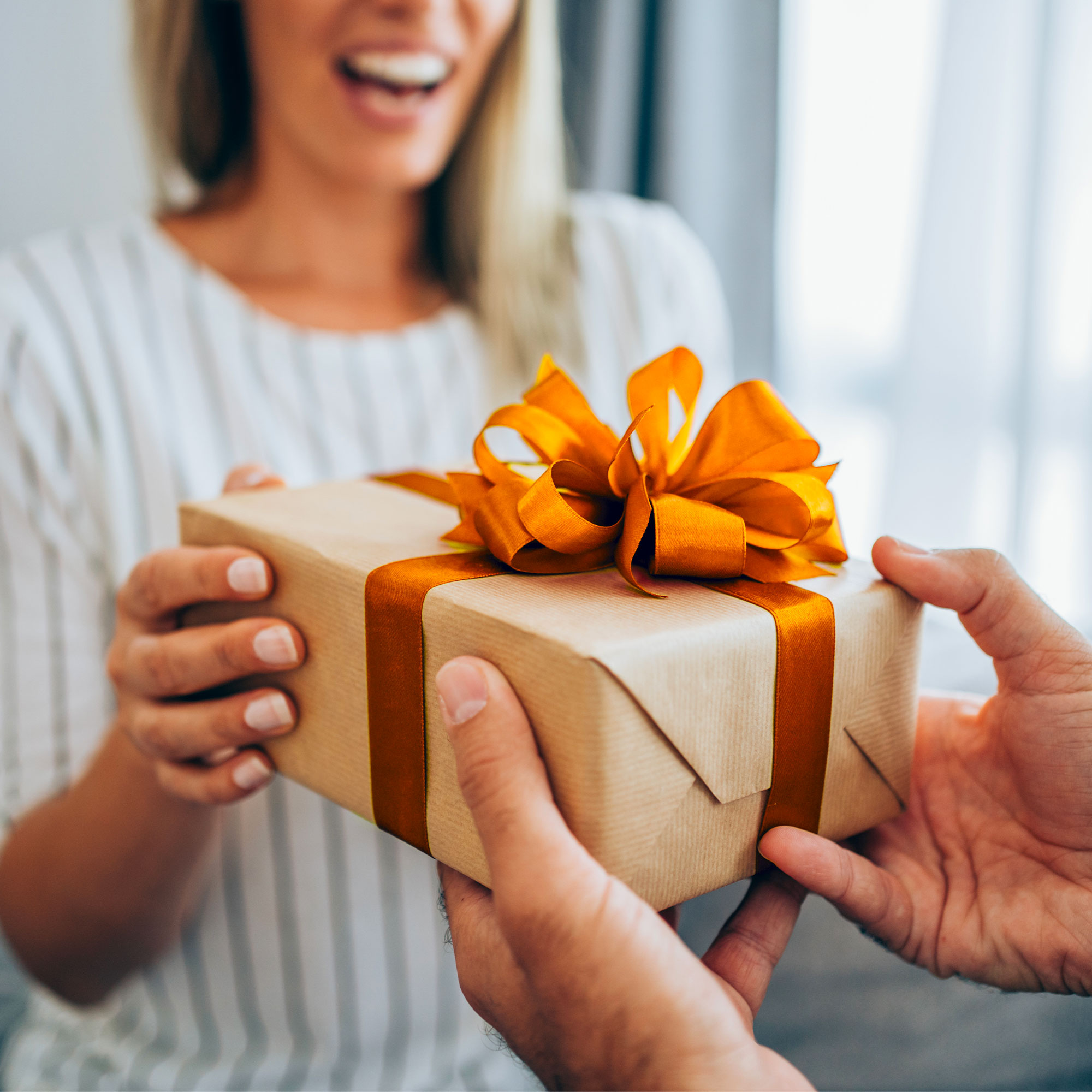 Woman smiles as she receives a gift box with an orange bow.