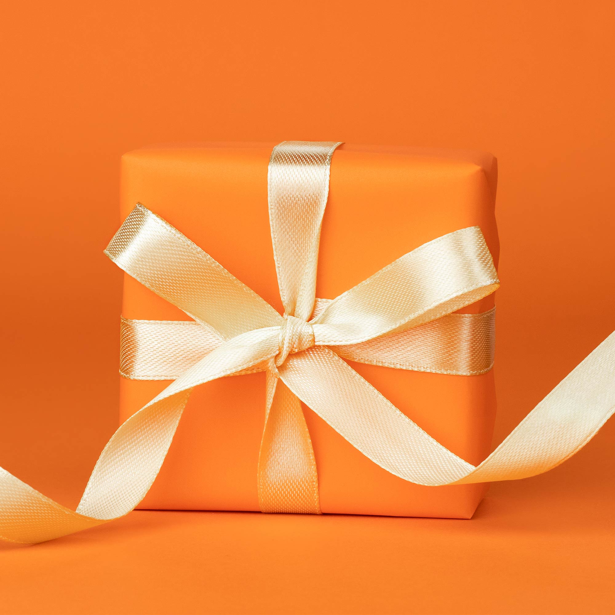 An orange gift box with white ribbon sits on a table.