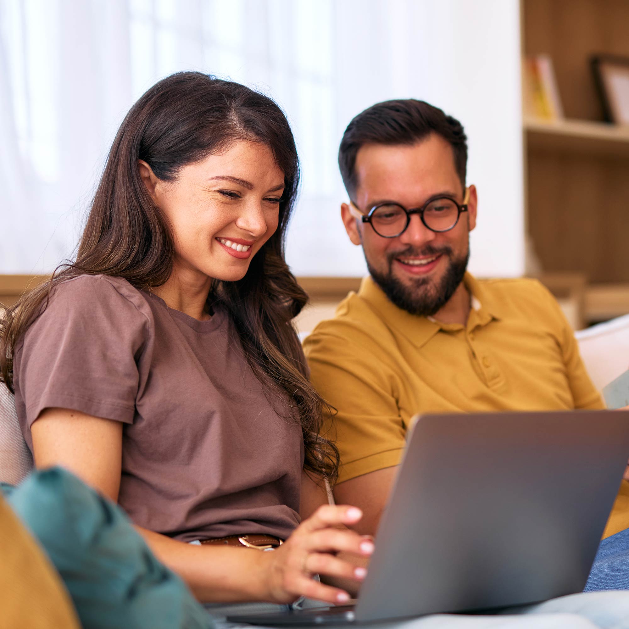 A man looks over a woman's shoulder and points at the computer screen.