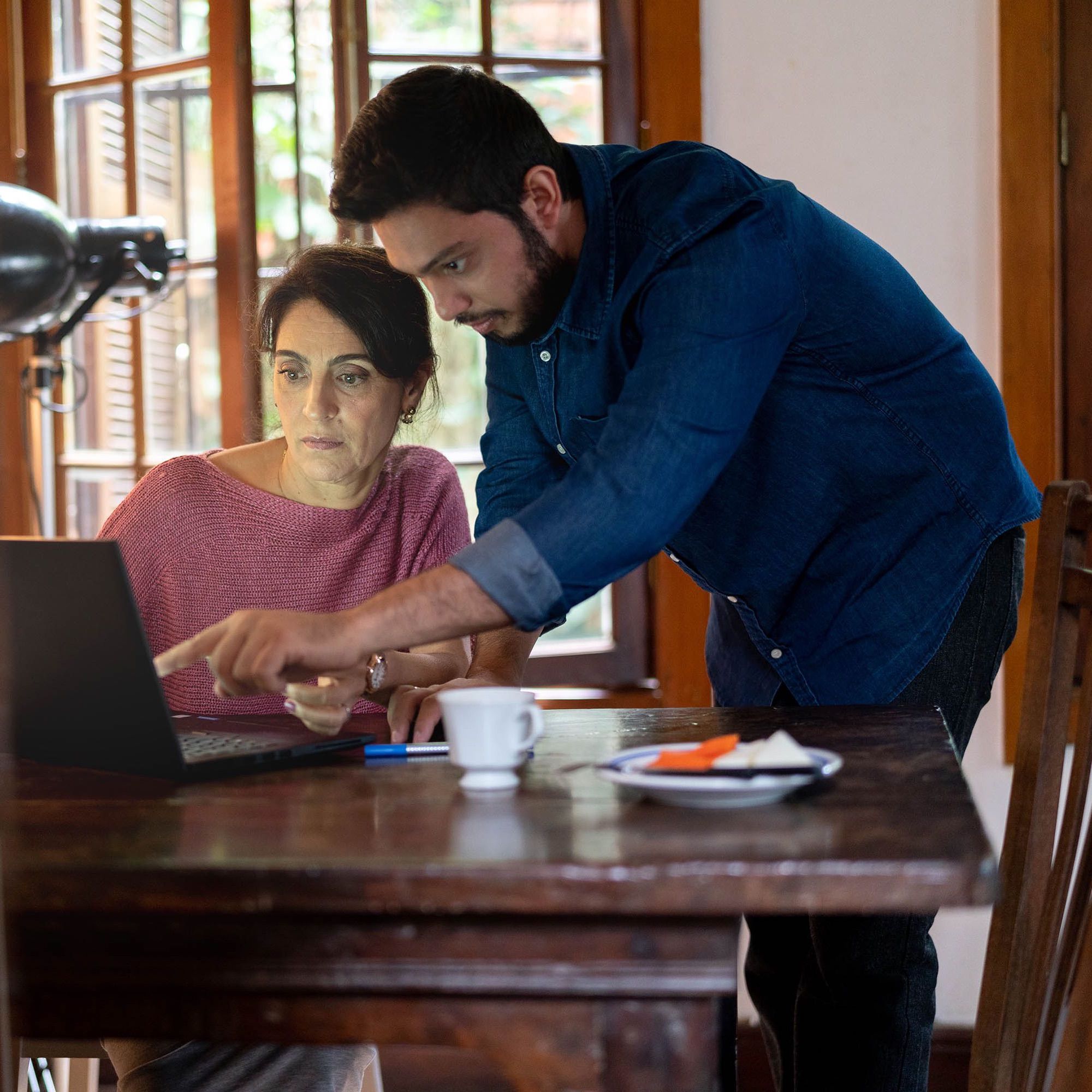 A man looks over a woman's shoulder and points at the computer screen.