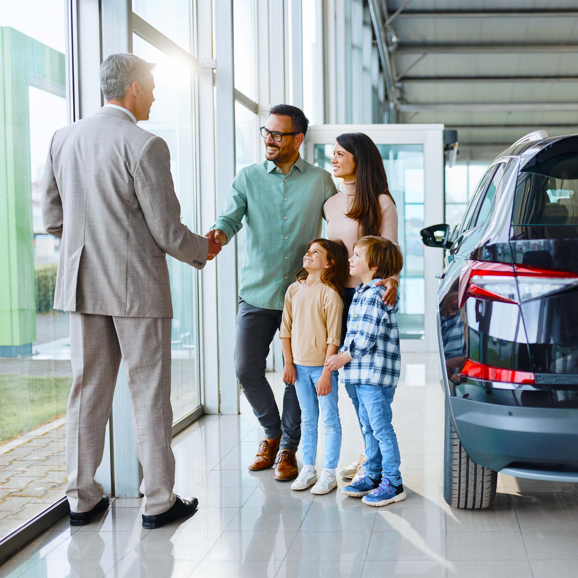 A family of four talking to a salesman at a car dealership.