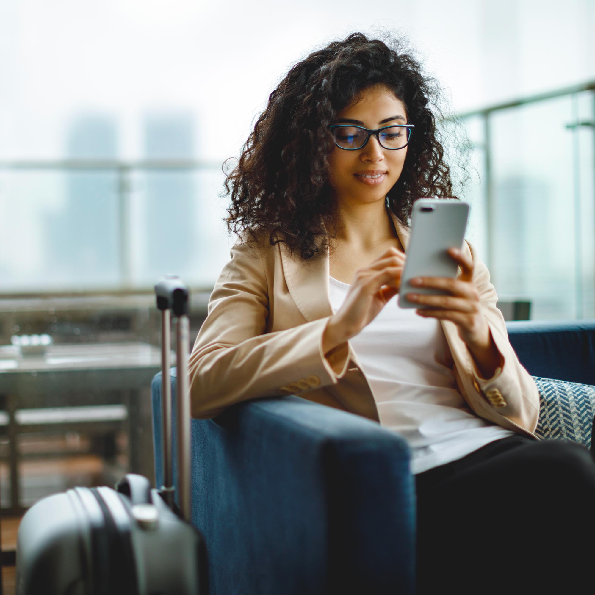 A woman wearing glasses uses her cell phone as she waits in an airport.