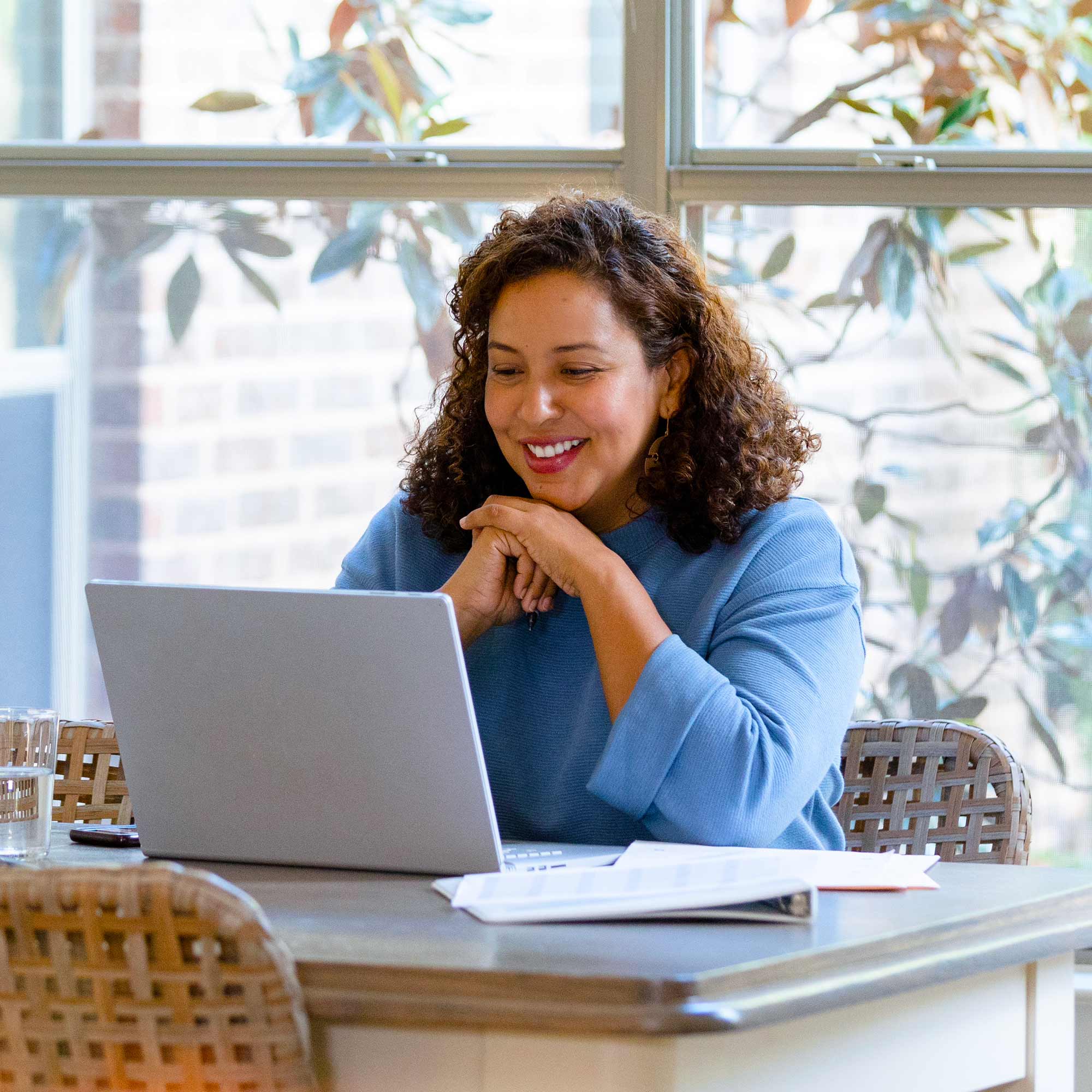 A woman sitting at a table wearing a blue shirt uses her laptop.