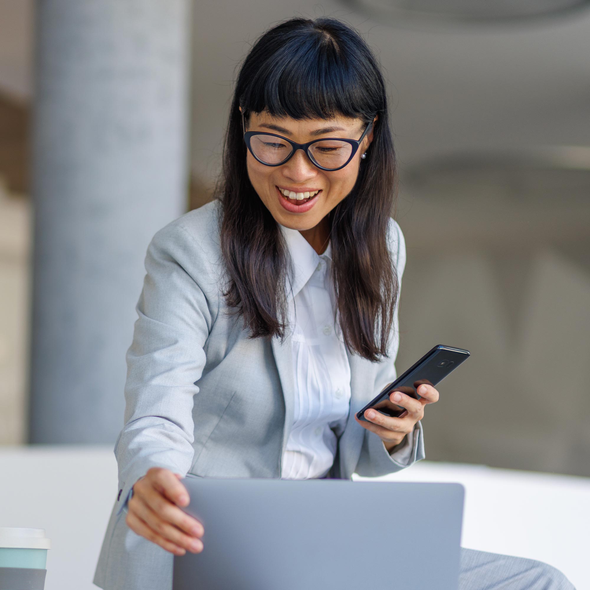 A man in a suit uses his cell phone and a laptop.