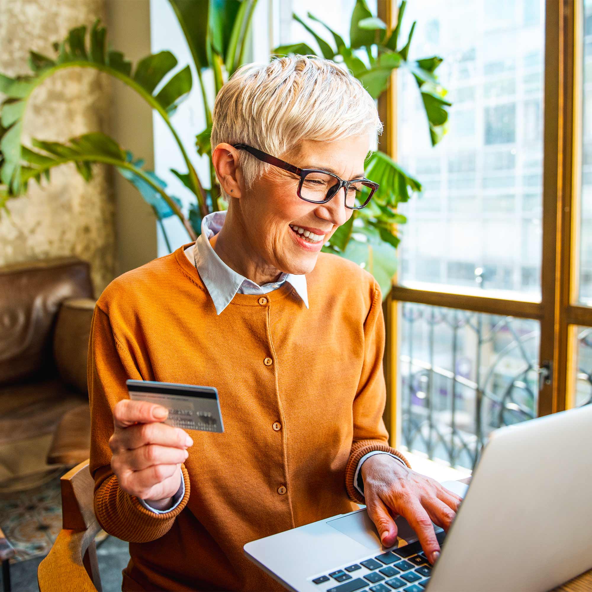 An older woman holds her credit card and looks at her computer.