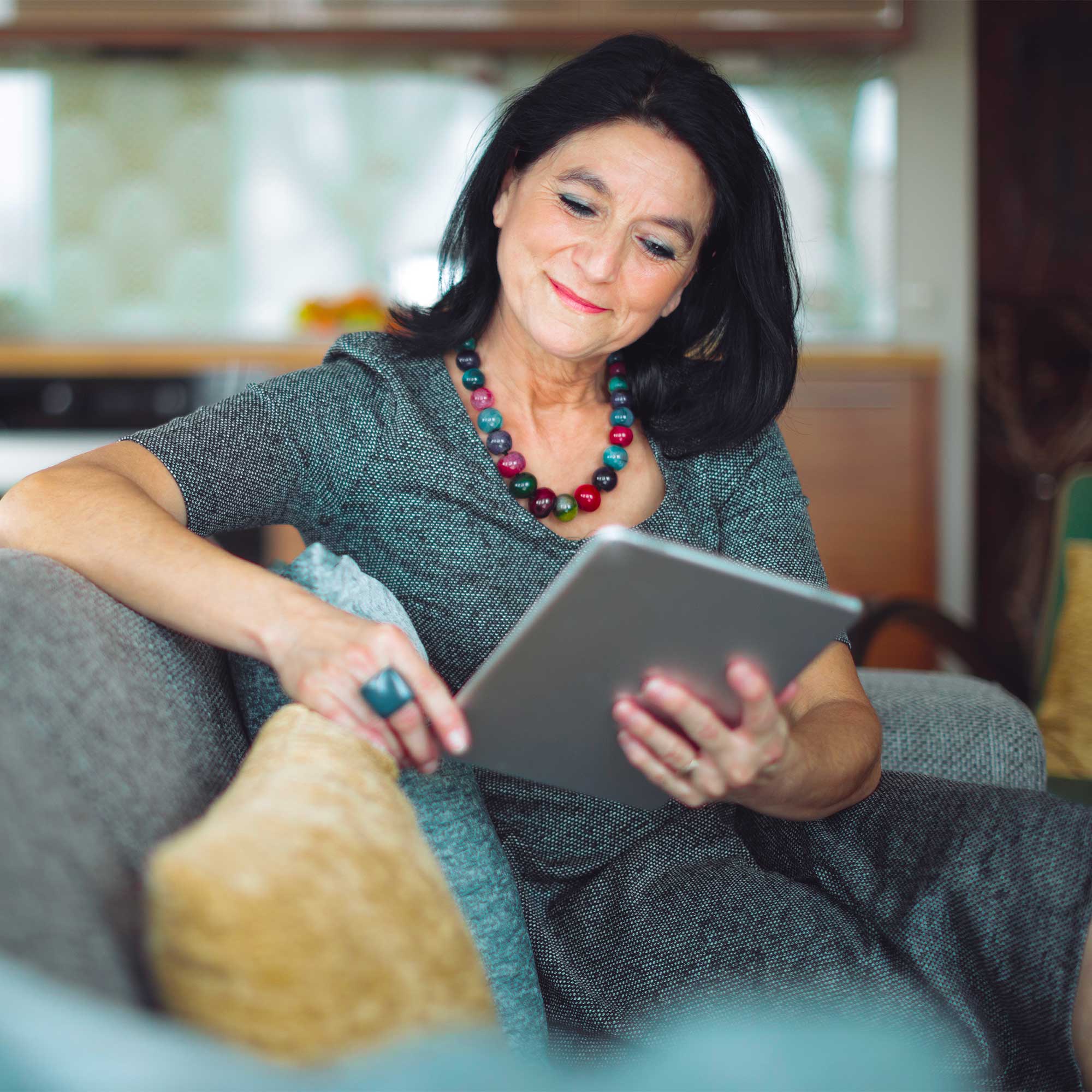 A woman sits on her couch using her tablet.