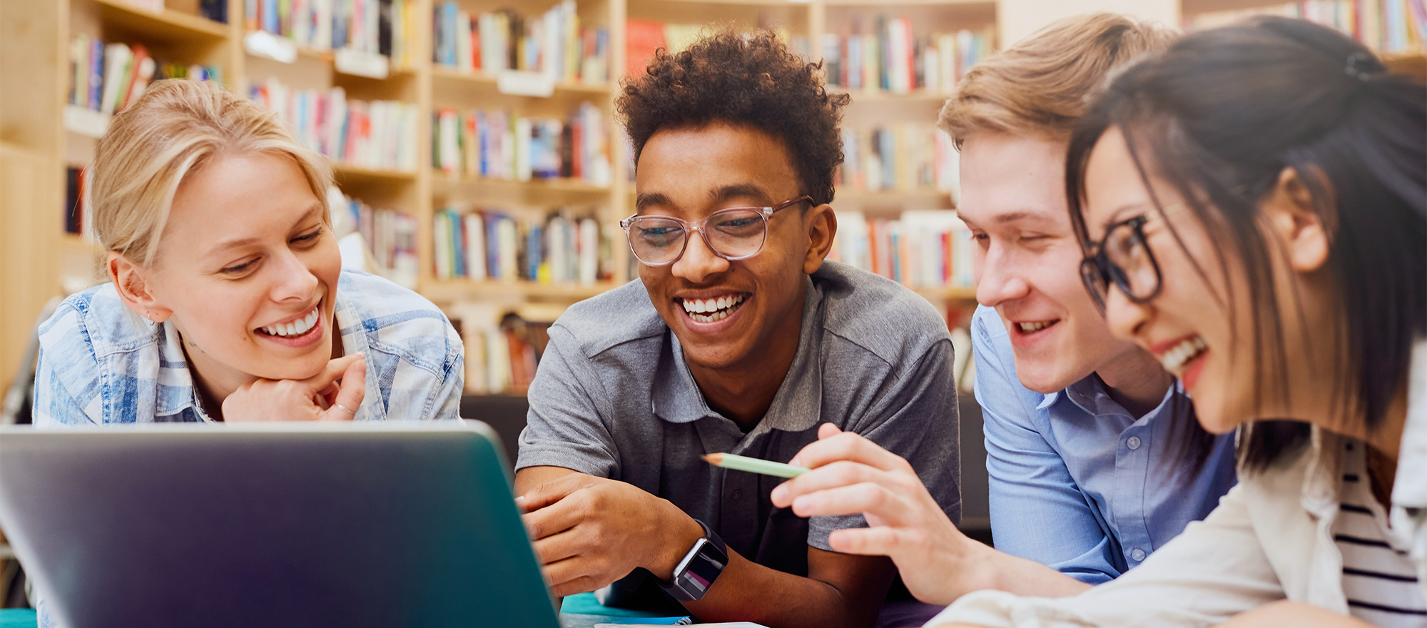 Four students are smile and laugh around a computer in the school library.