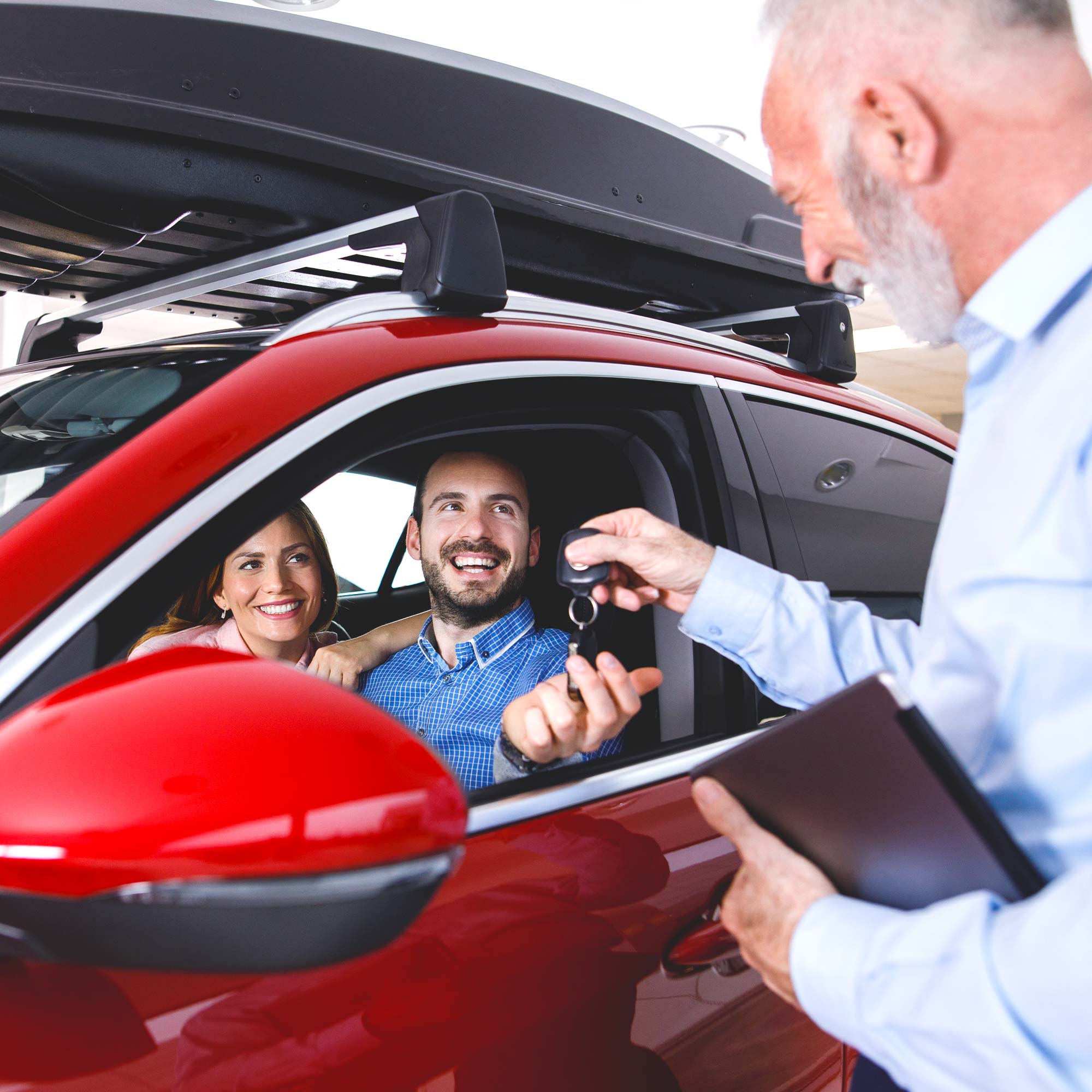 A man and woman smile at the salesman as they sit in a brand new red car.