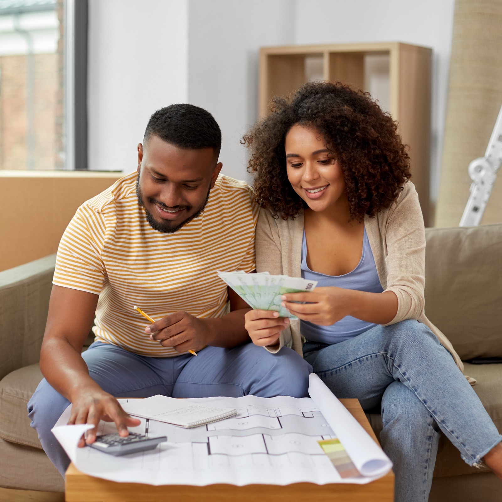 A couple looks at paint samples and examine a blueprint while they sit on their couch.