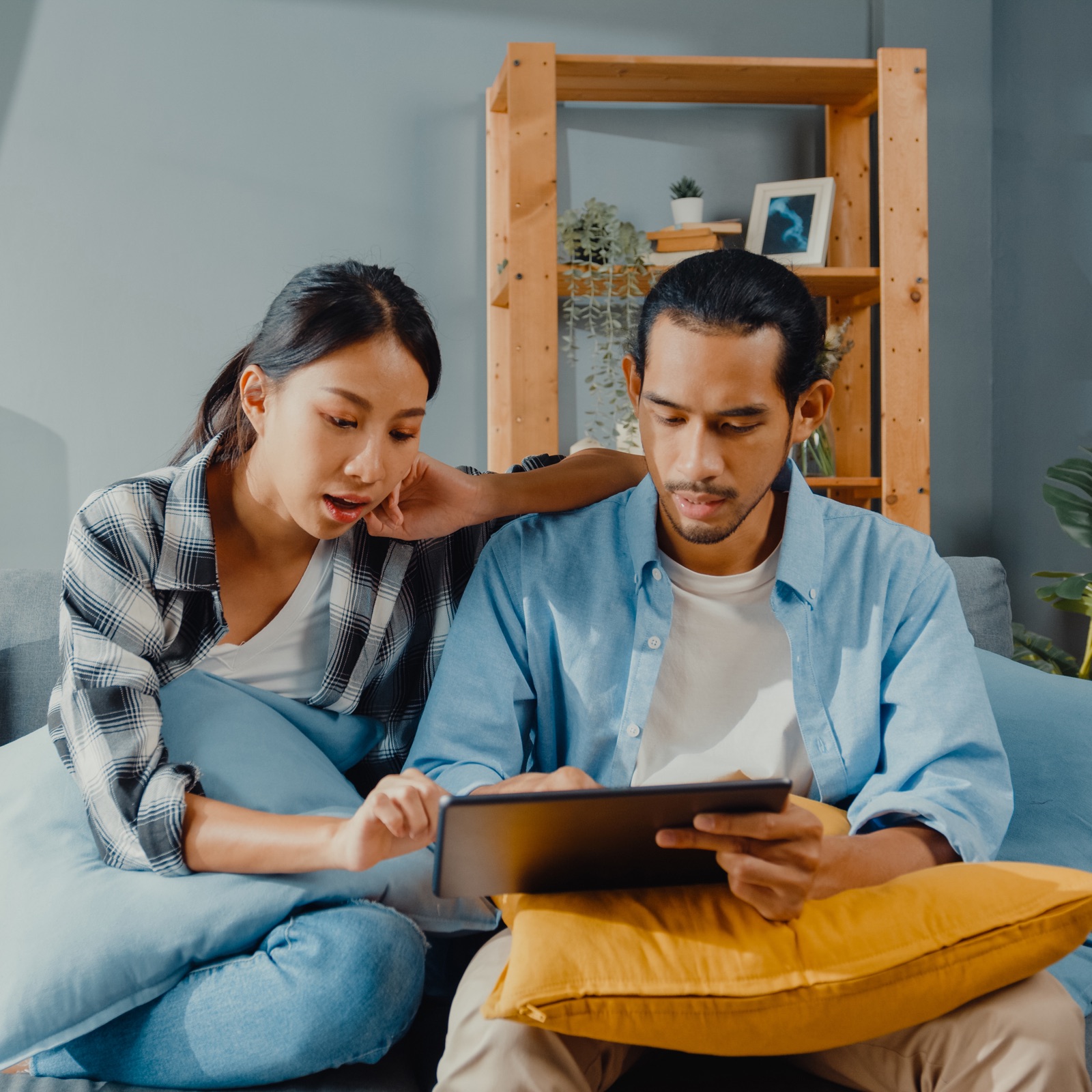 Man and woman looking at a tablet as they sit on their couch.