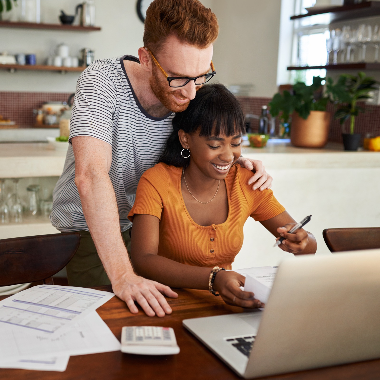 Man looking over a woman's shoulder while she is working at her computer.