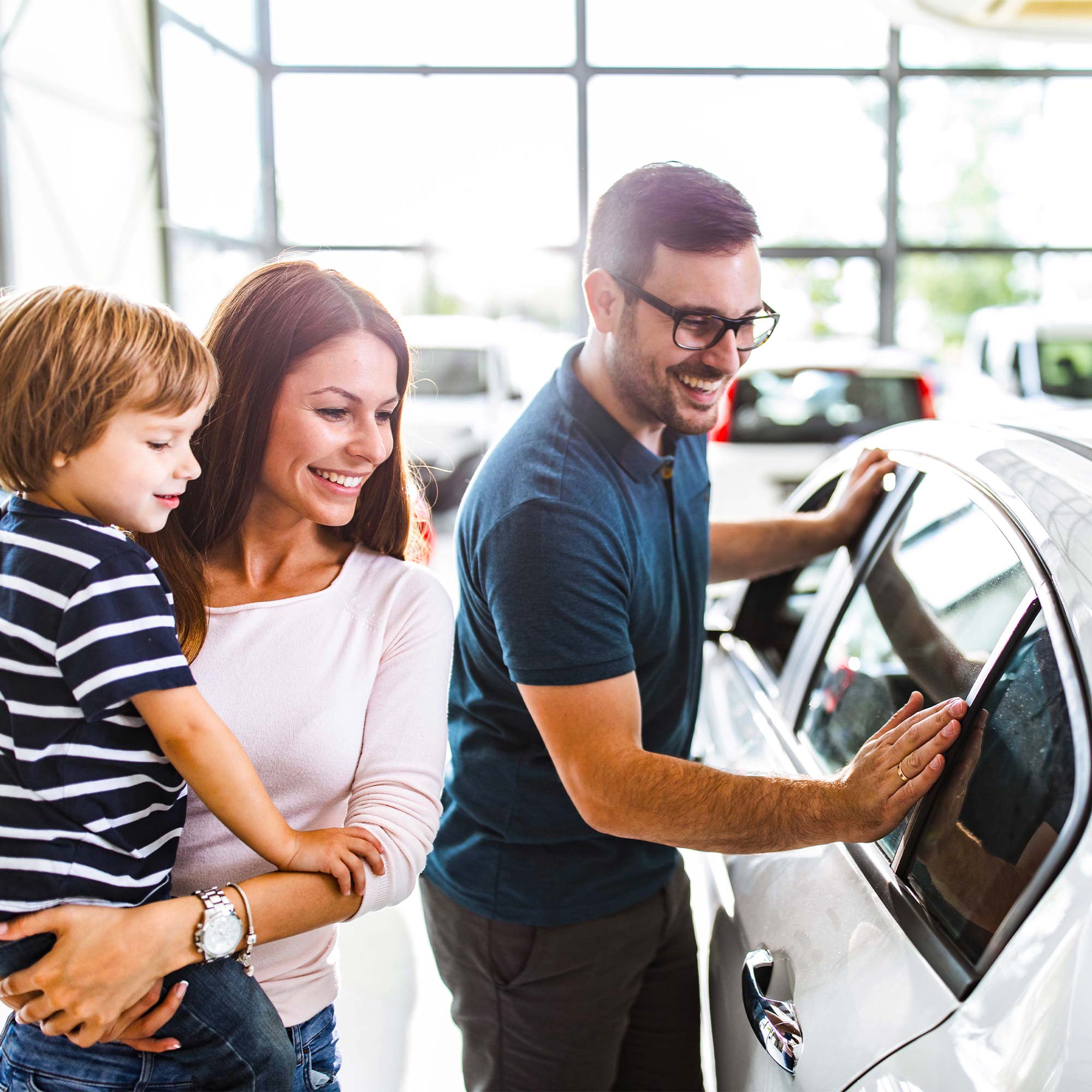 A man, woman and child are shopping for a car at the dealership.
