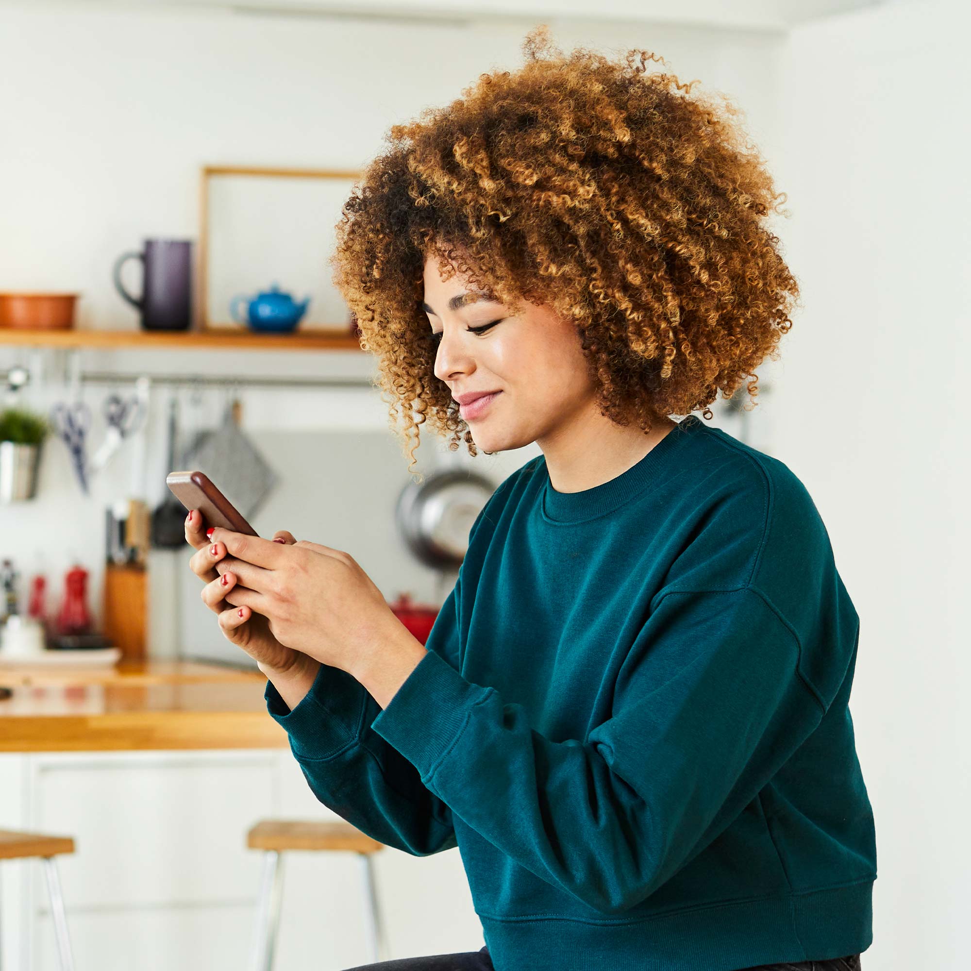 A woman sits at a table and uses her phone to view the Plaid app