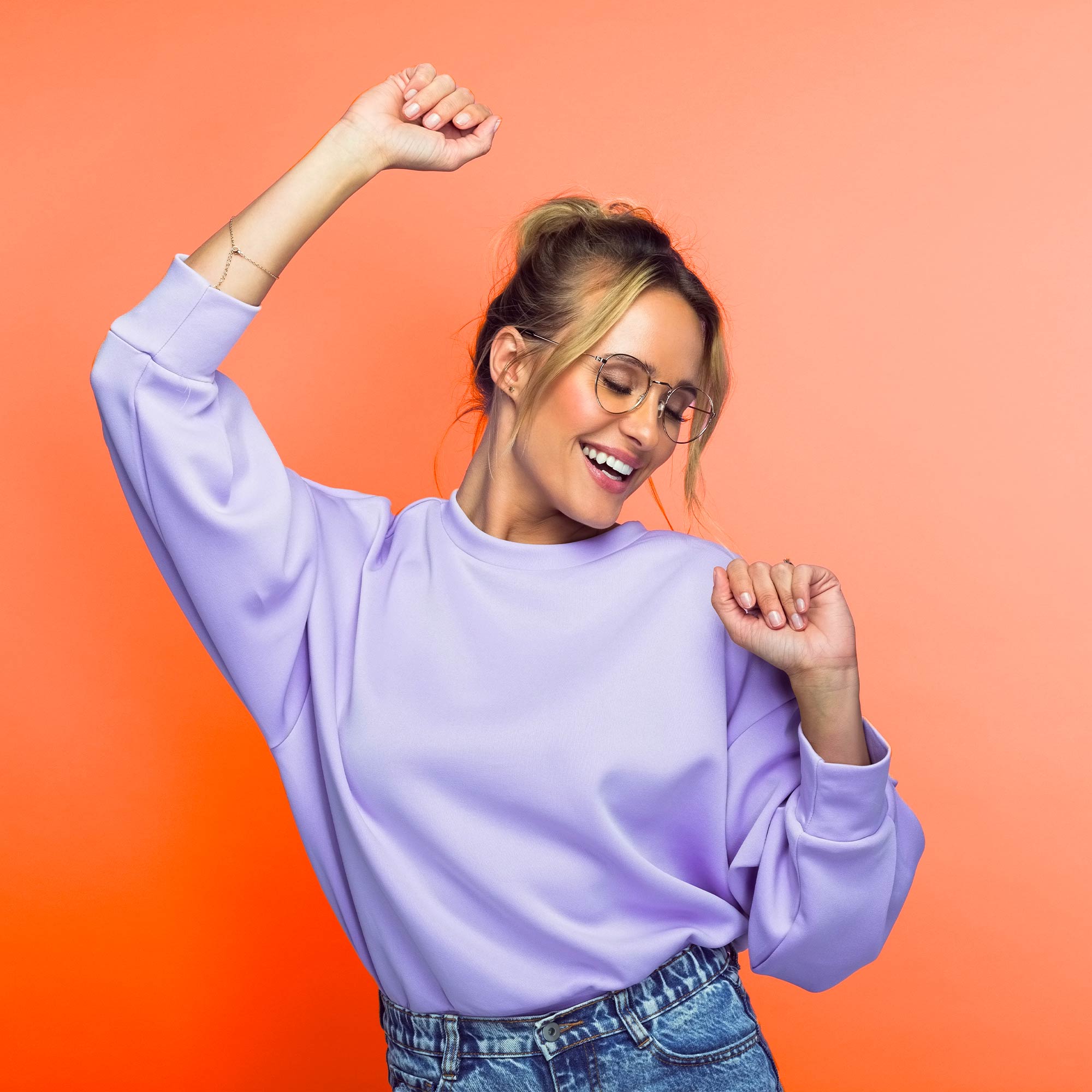 A girl wearing a purple shirt dances in front of an orange background.