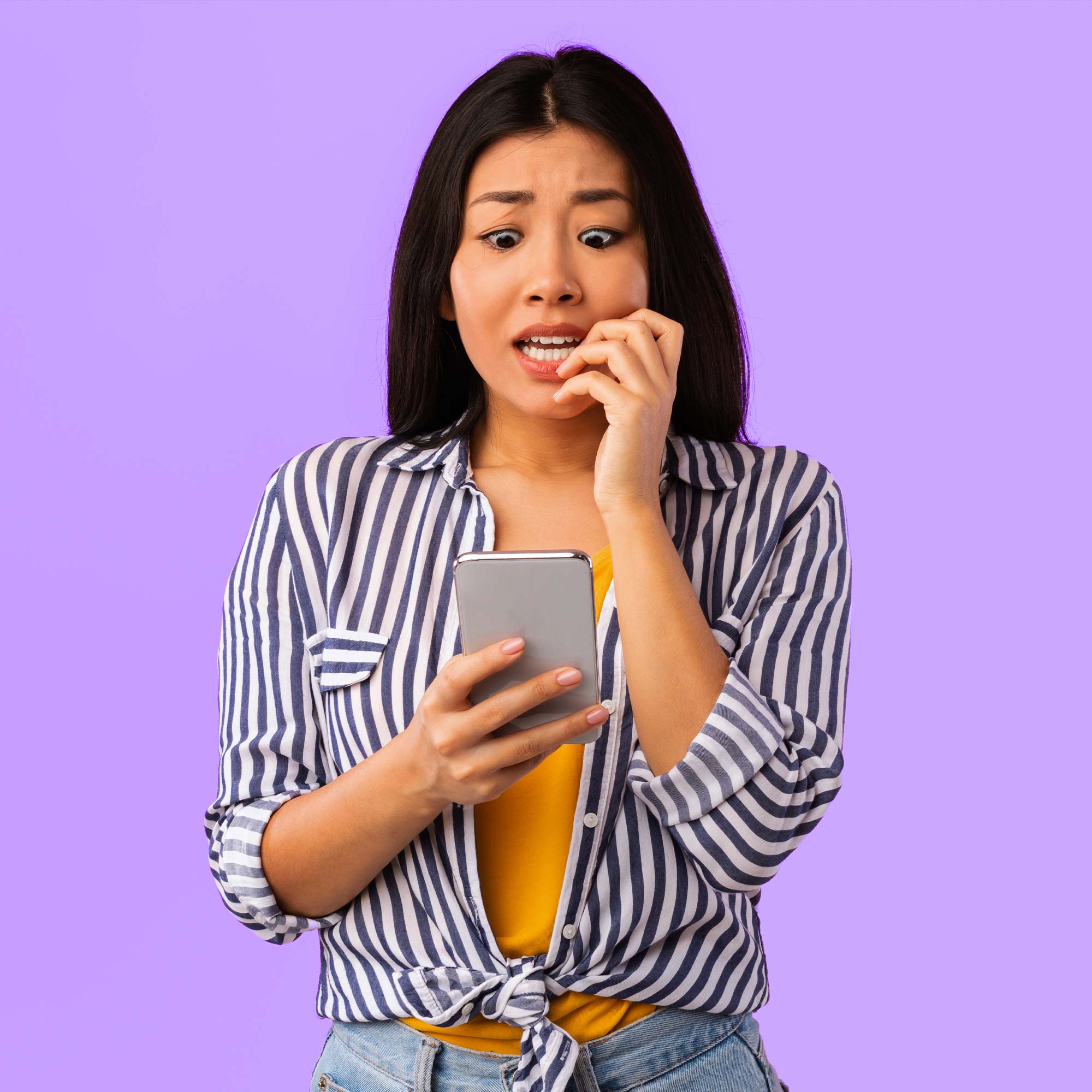A woman wearing a striped shirt looking very concerned at her phone.