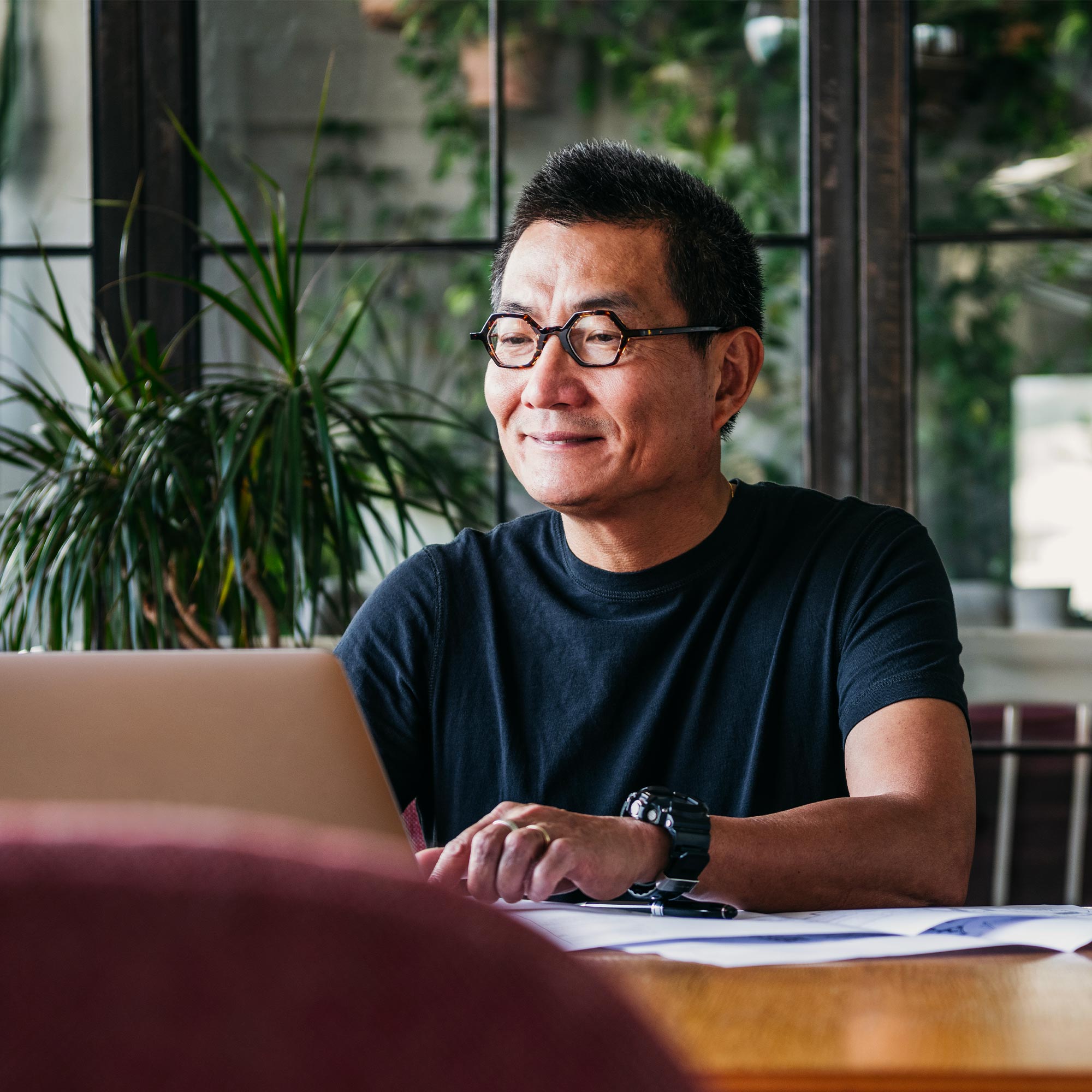 A man wearing glasses uses a laptop at the dining room table.