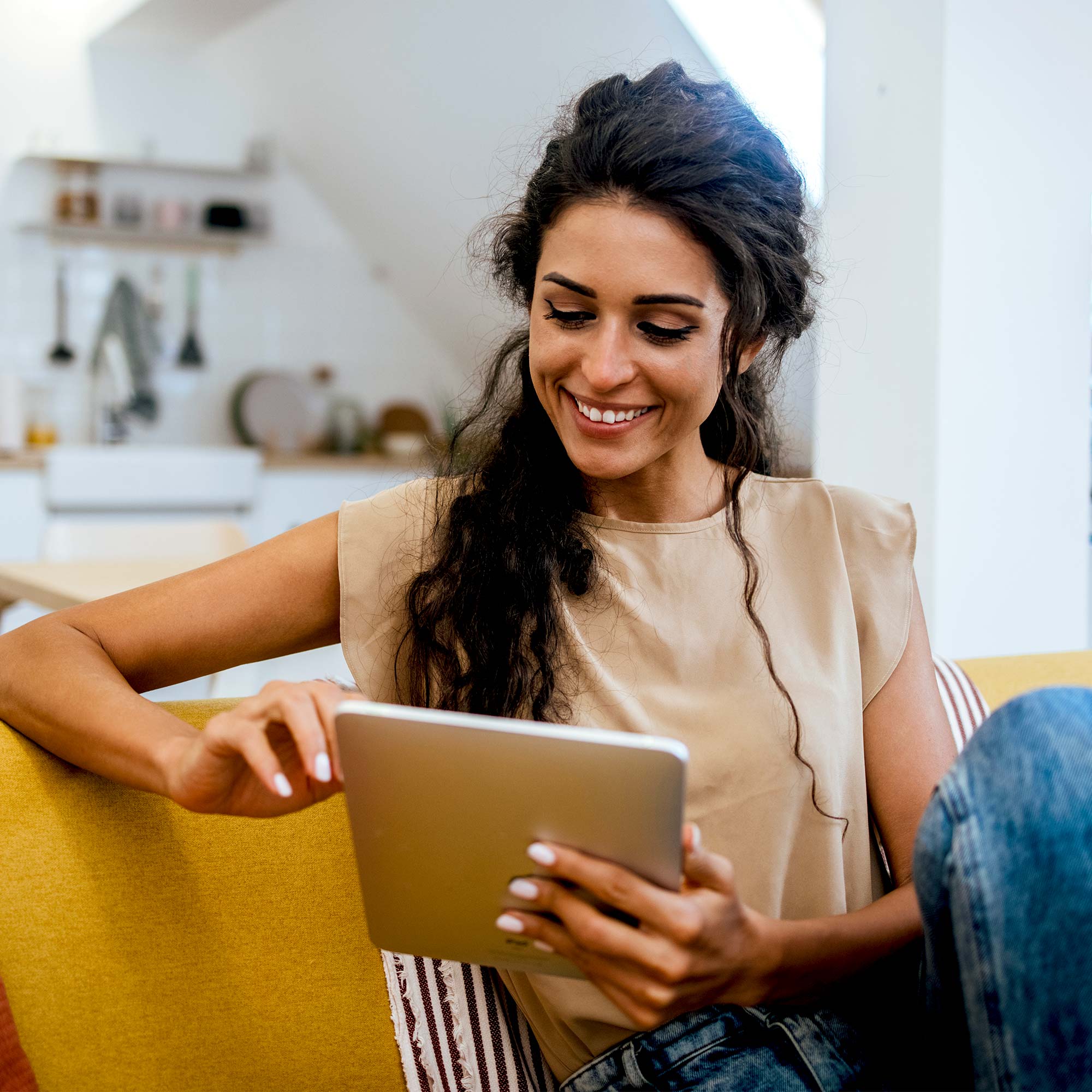 A woman sitting on a couch smiling and using her tablet.