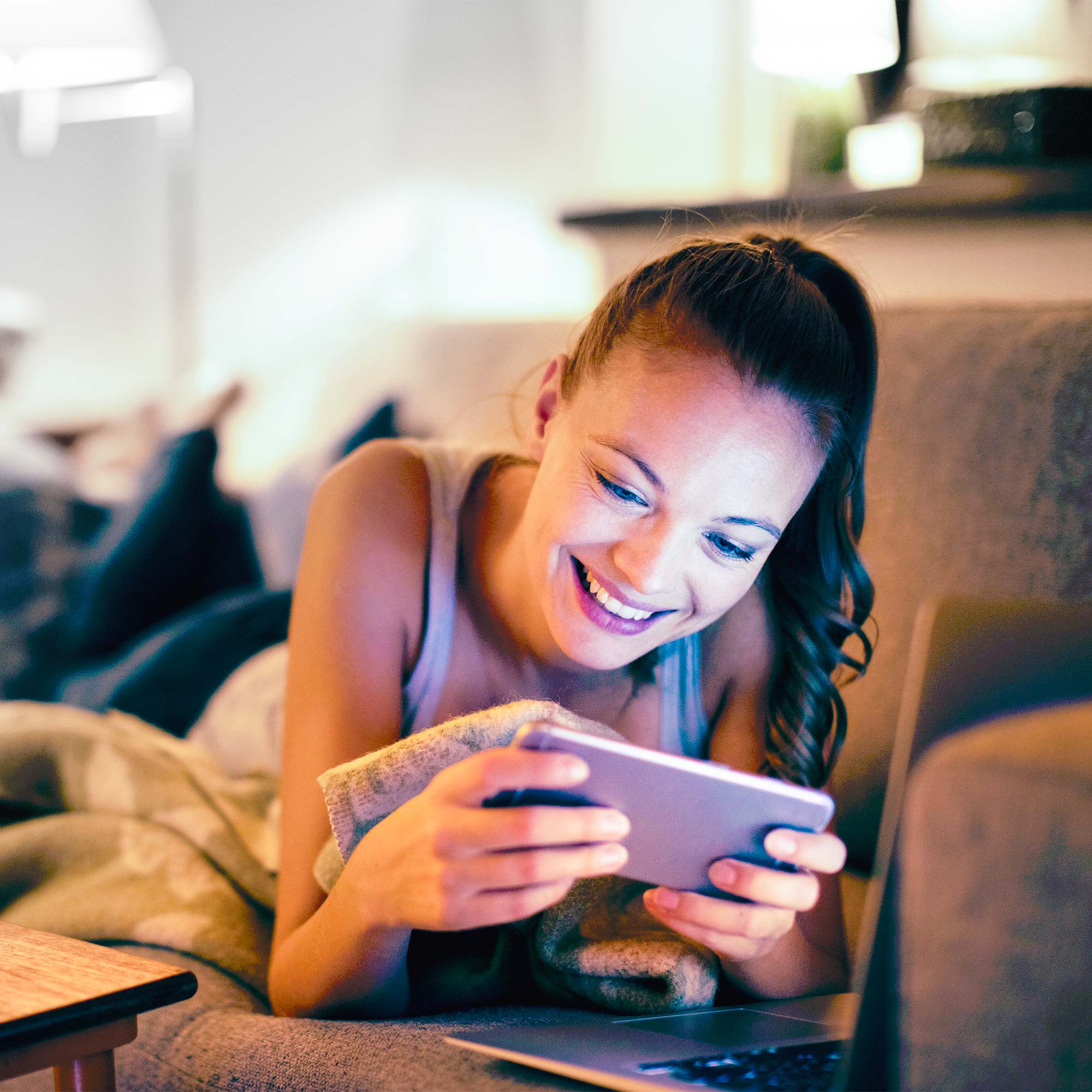 A woman lays on the couch and smiles at her phone.