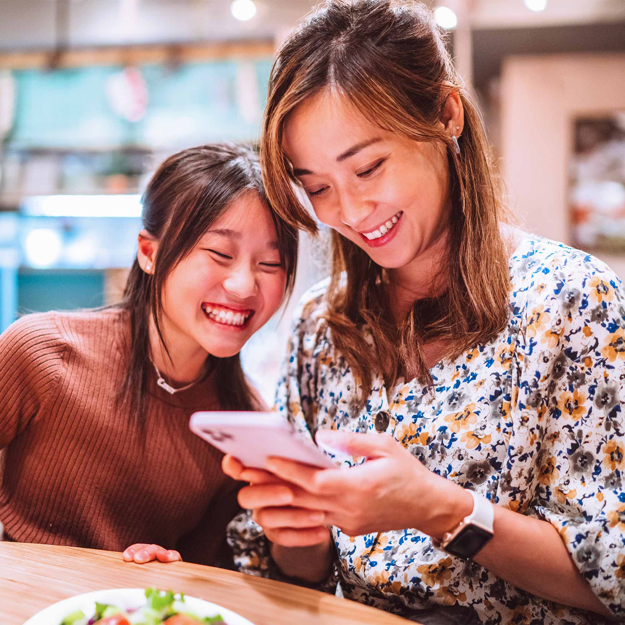 A woman in an orange shirt looks out from the balcony with a cup of coffee in hand.