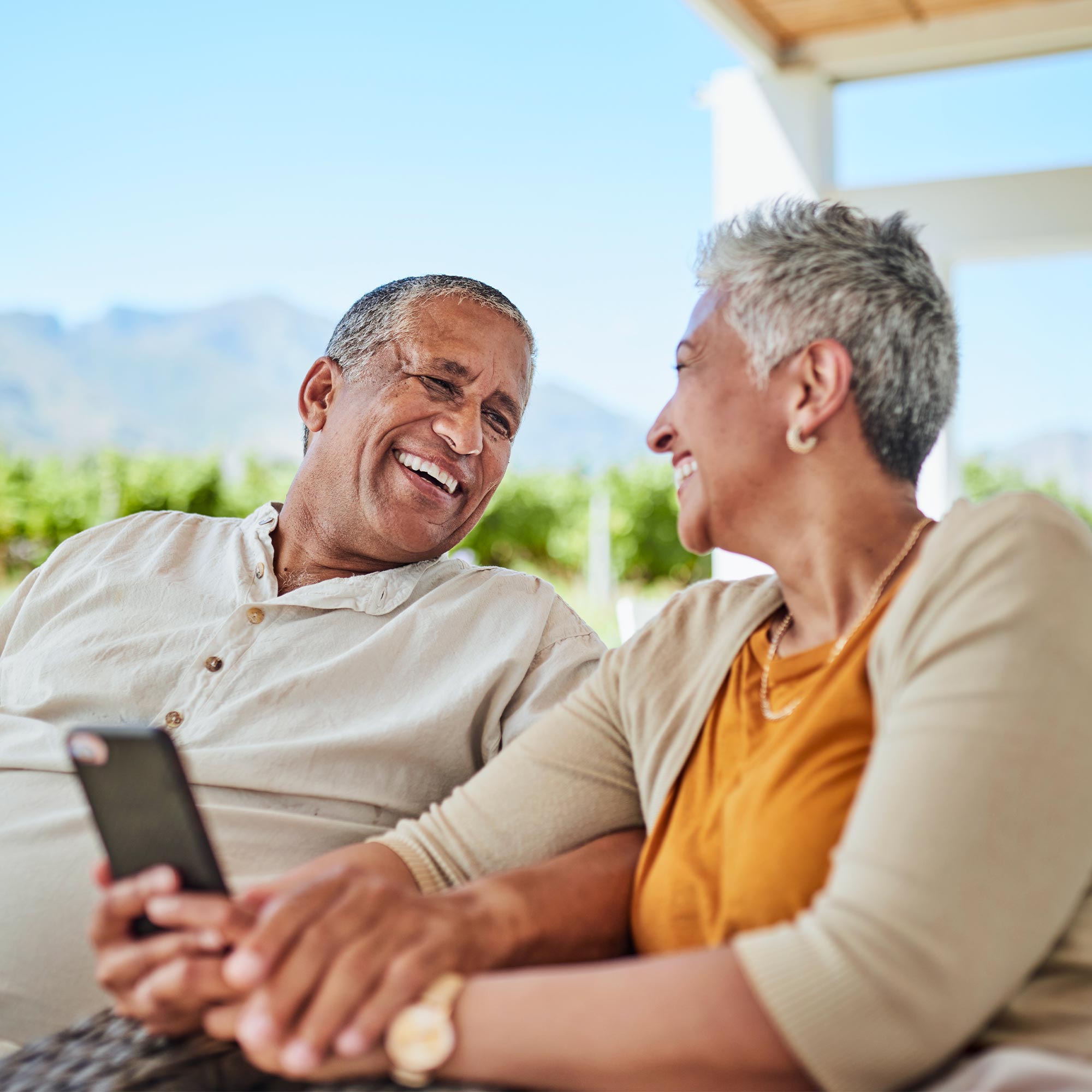 Two elders sitting outside looking at each other as they smile.