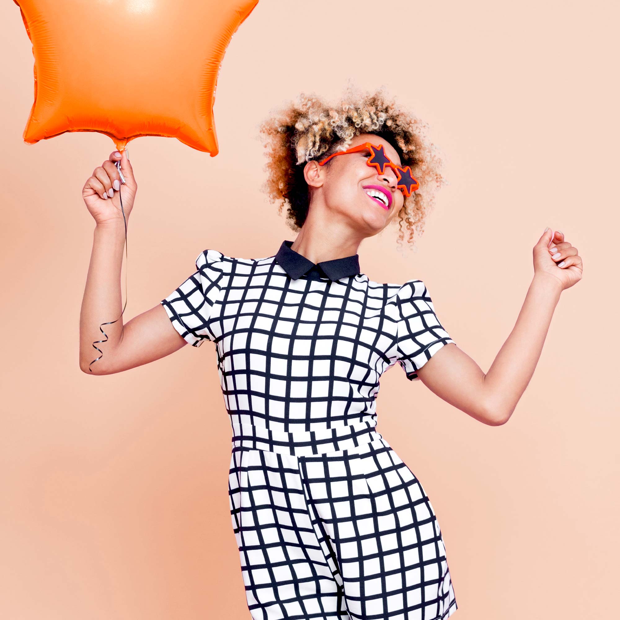 A woman holdis an orange star-shaped balloon and smiles.