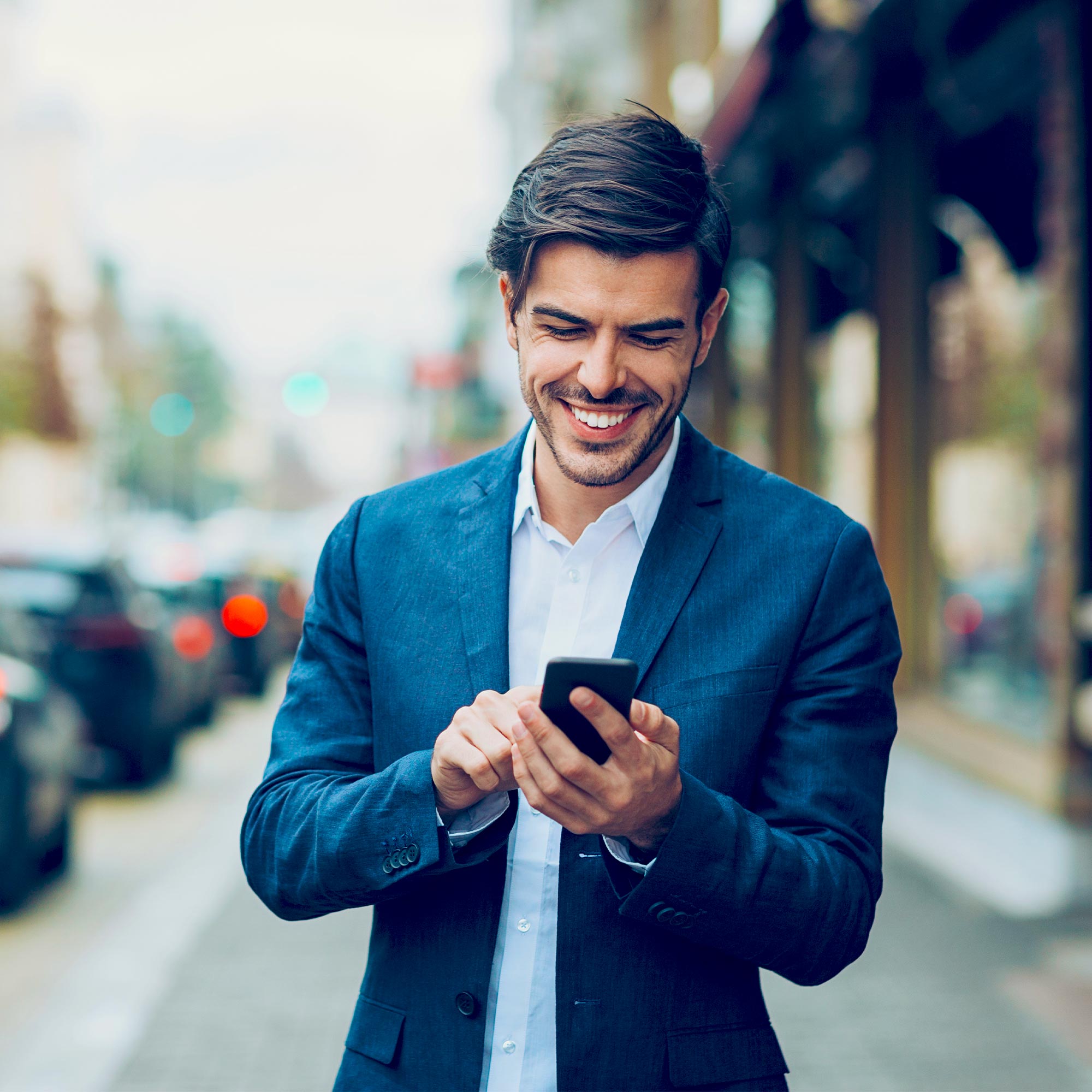 A man wearing an orange jacket smiling and looking at his phone.