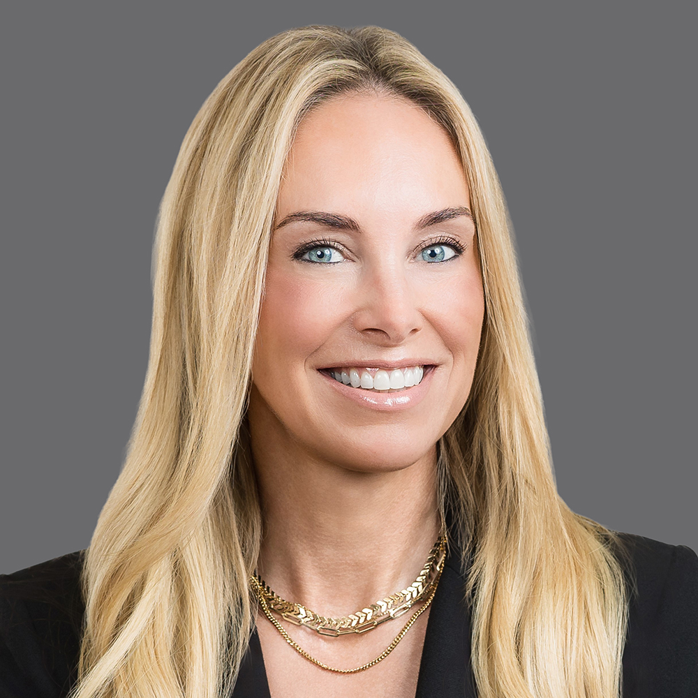 a woman with blonde hair wearing a black blazer and gold necklace