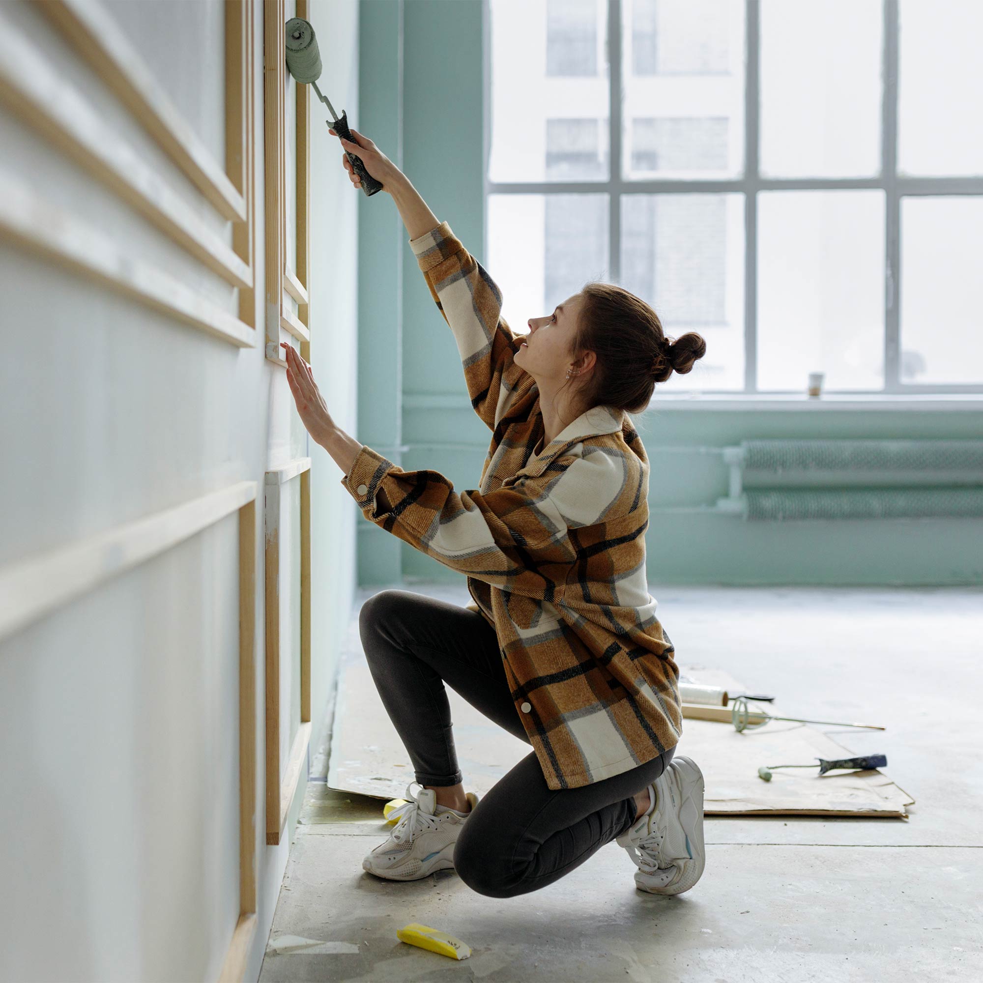 A woman painting the wall as she kneels.