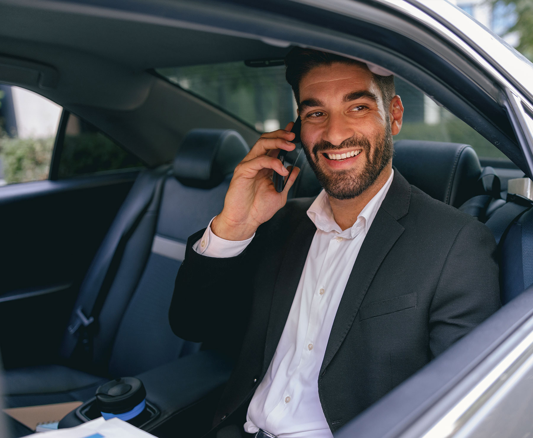 A businessman sitting in the back of a car talking on a phone