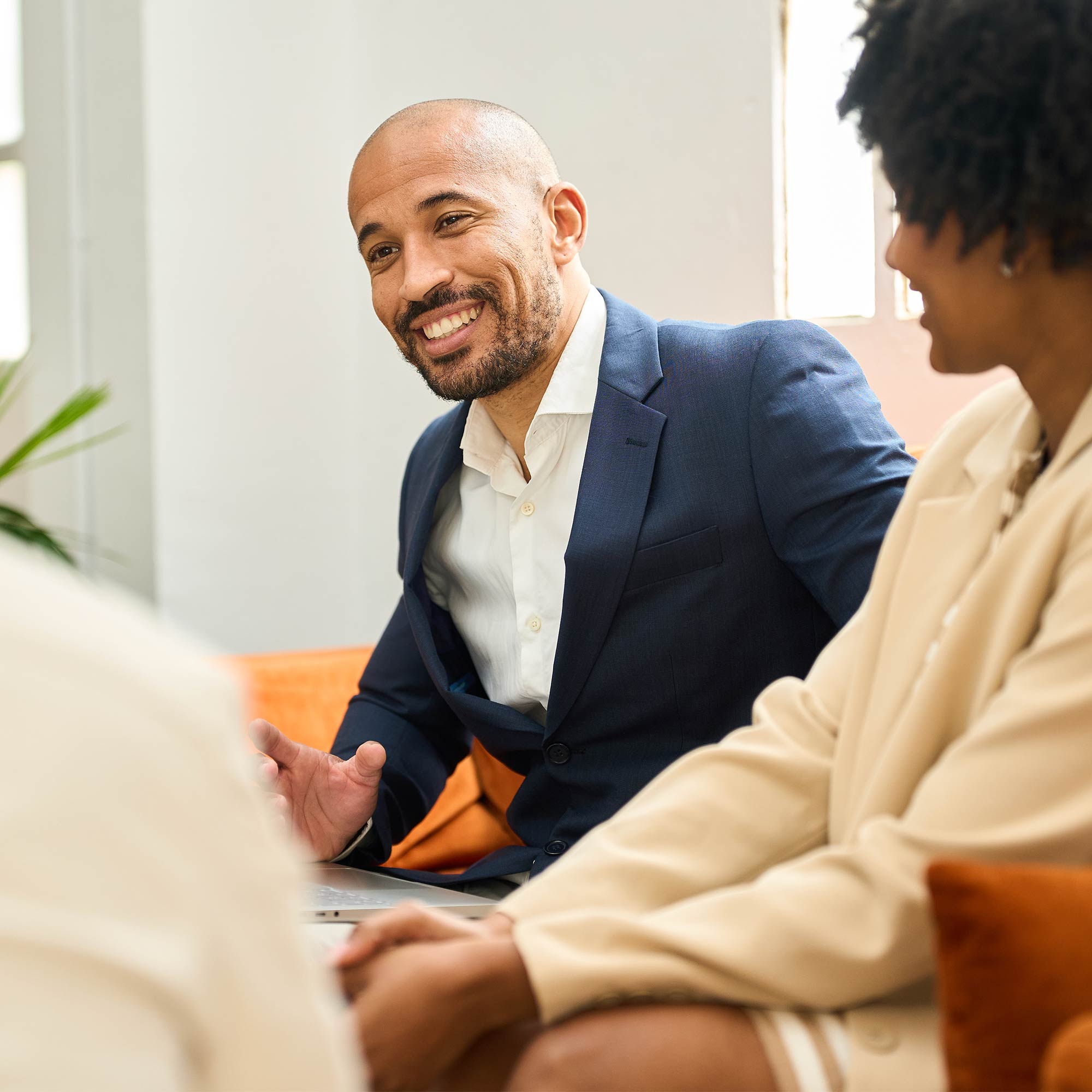 A professionally dressed man sits at a table working on a laptop.