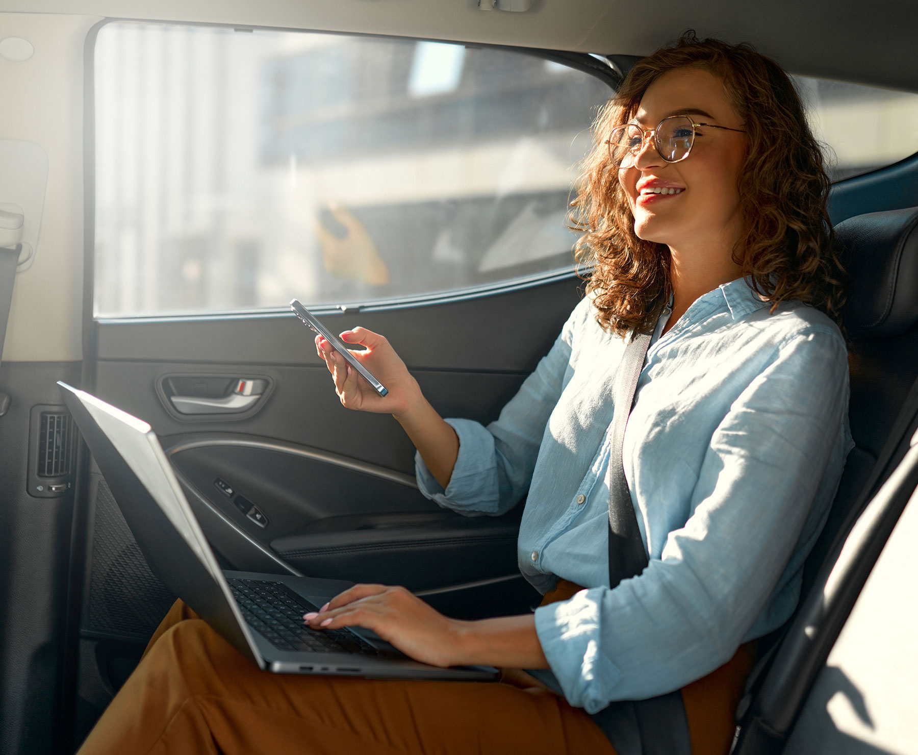A woman sitting in the back of a car using her laptop