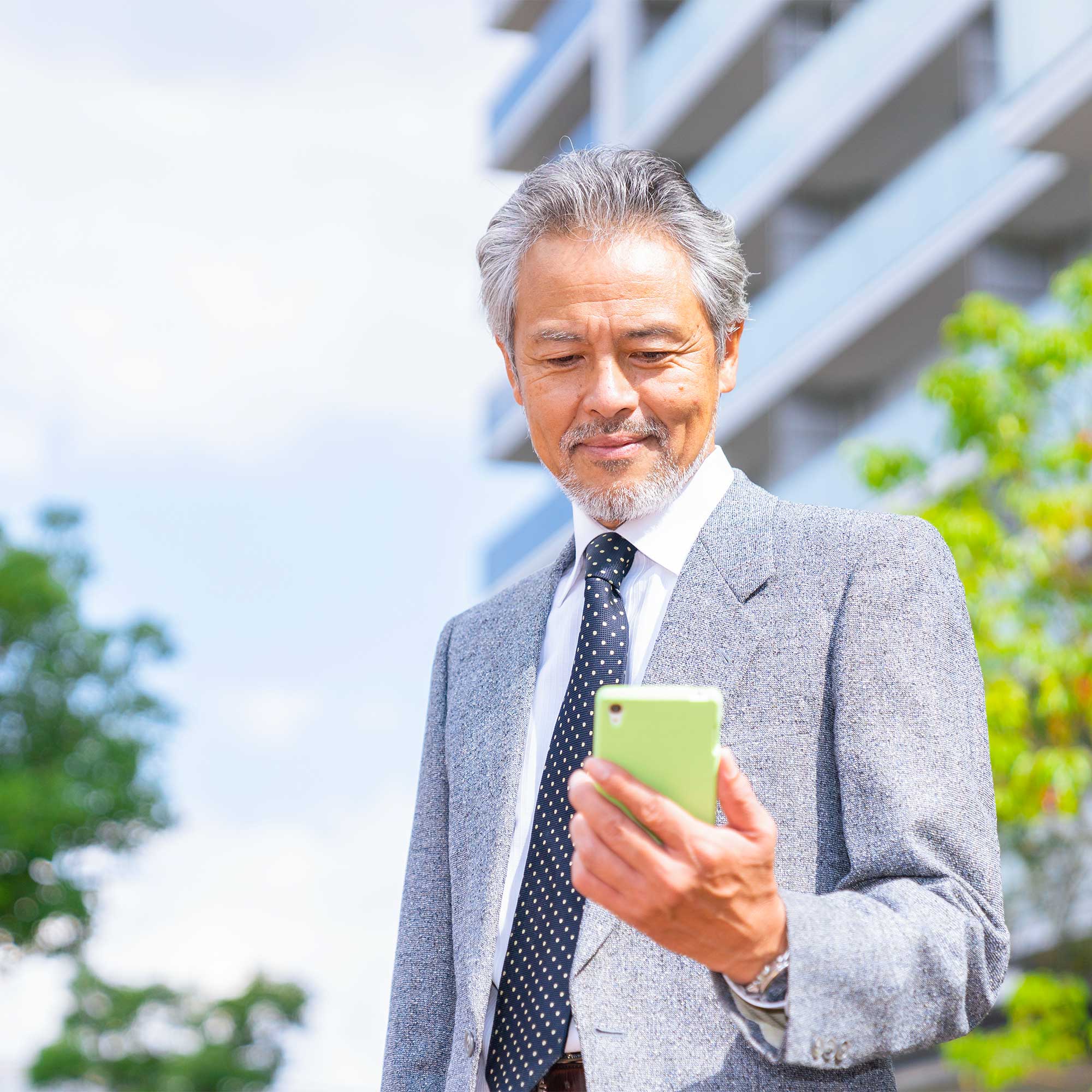 Professionally dressed man standing outside of an office building while looking down at his phone